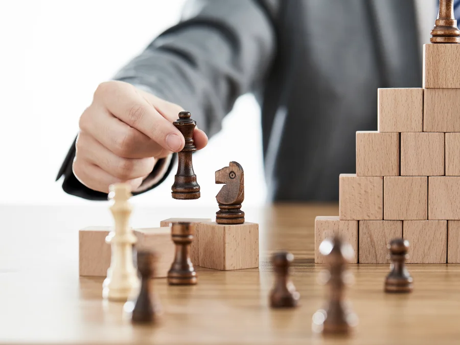 Businessman moving a chess piece beside a staircase of wooden blocks